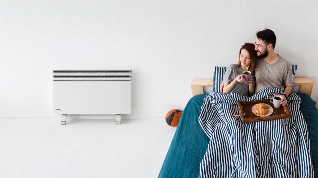 Couple enjoying breakfast in bed beside a wall-mounted heater.