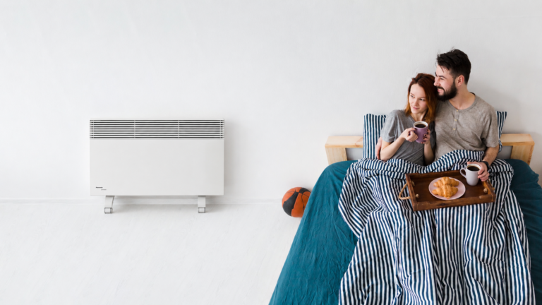 Couple enjoying breakfast in bed beside a wall-mounted heater.