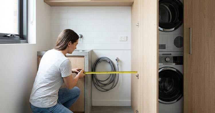 Woman measuring a laundry room cabinet with a tape measure.