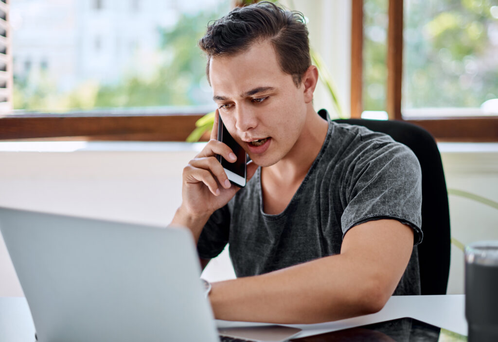 man calling on phone while using a laptop